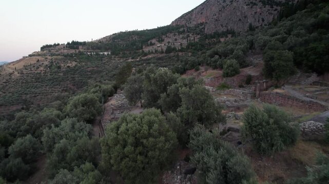 Aerial view of the ancient archaeological site of Delphi surrounded by olive groves and rugged mountains in Delphi, Greece.