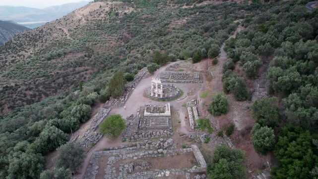 Aerial view of the ancient Tholos of Athena Pronaia ruins surrounded by olive groves and rugged hillsides in Delphi, Greece.
