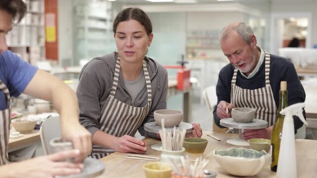Elderly man, young woman and young man, at work table create handmade ceramics in ceramics workshop 