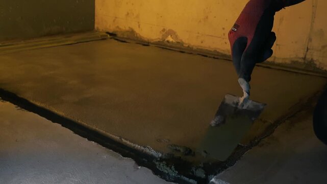 Close up view of a skilled builder's hand using a trowel to apply and smooth fresh cement mixture, meticulously repairing and leveling a damaged floor during renovation