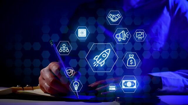 A person writes on a notepad at night while surrounded by digital icons representing business concepts. The setting has a dark background with blue lighting.