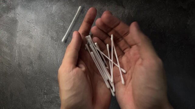 Cupped hands holding pile of white cotton swabs overhead