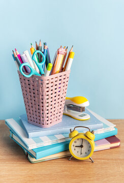 School supplies and alarm clock on desk with notebooks