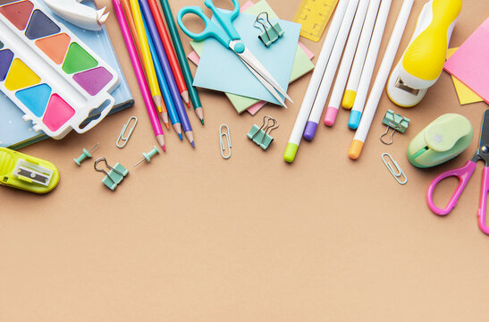 Colorful school and office supplies border on brown background