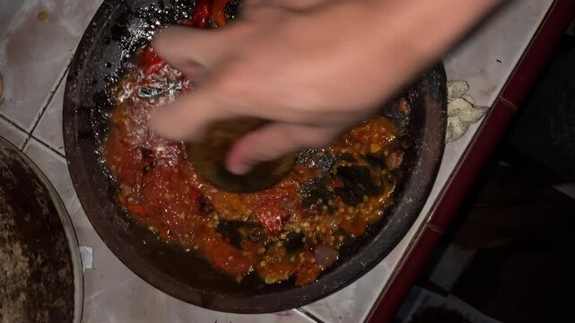 Hand grinding chili paste with pestle in stone mortar