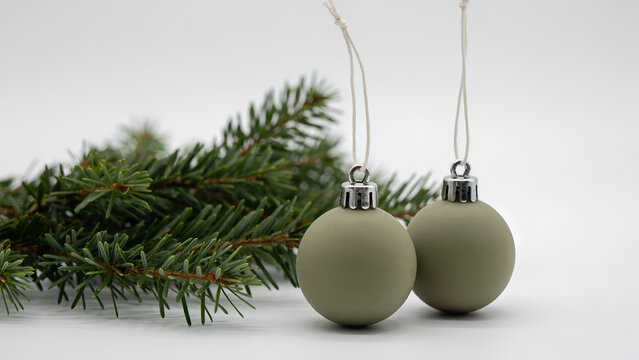 Two matte sage green christmas baubles hanging with pine branches isolated on white background