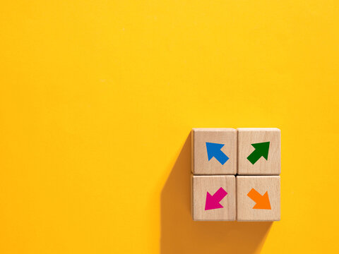 Four wooden cubes showing colorful arrows pointing in different directions on yellow background