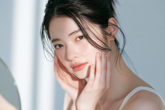 鏡の前で肌のケアをしているアジア人女性。美容、スキンケア用素材