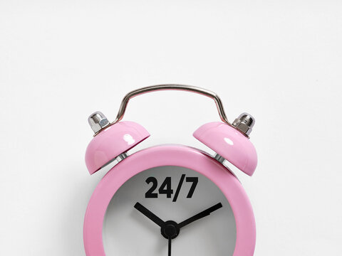 Pink alarm clock showing 24/7 service on white background