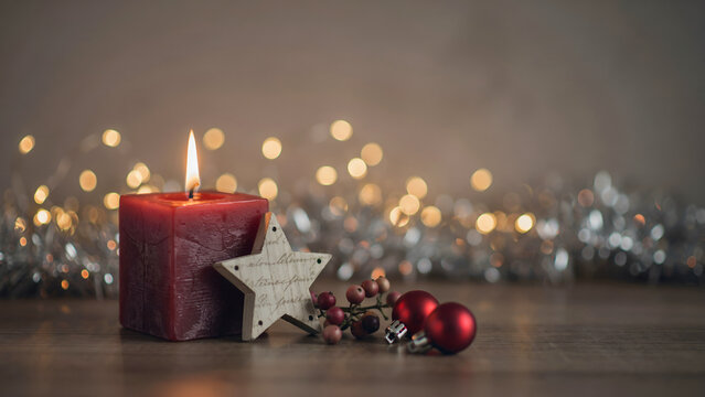 A festive christmas setting featuring a burning red candle, a decorative wooden star, and small red baubles against a blurred background of fairy lights