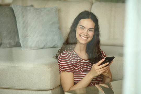 Happy teenage girl holding phone looking through a window