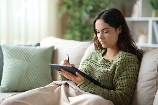 Young woman handwriting on tablet covered with a blanket in winter