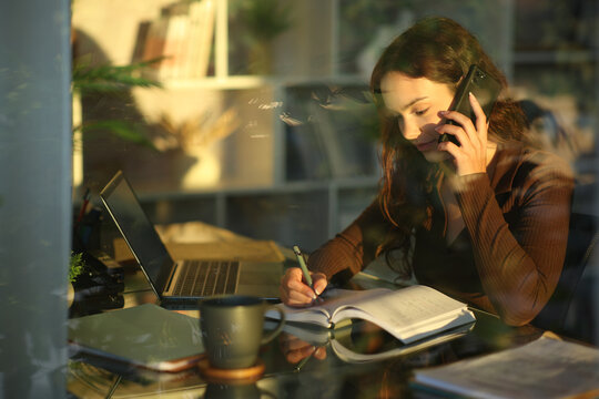 Young telecommuter talking on phone and writing notes in agenda
