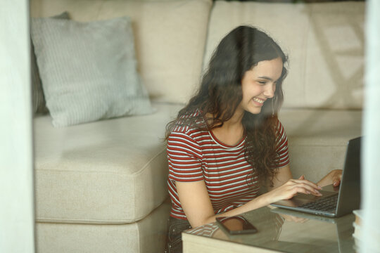 Happy teenage girl using laptop through a window