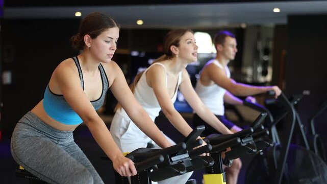 Sportive young woman doing spin bike exercises in well-equipped gym during training session 