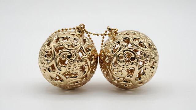 Two ornate gold christmas ball ornaments with intricate filigree patterns connected by a small golden chain isolated on white background