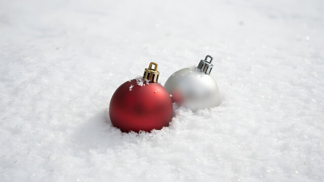 Two christmas baubles, one red and one silver, resting in fresh white snow outdoors during winter