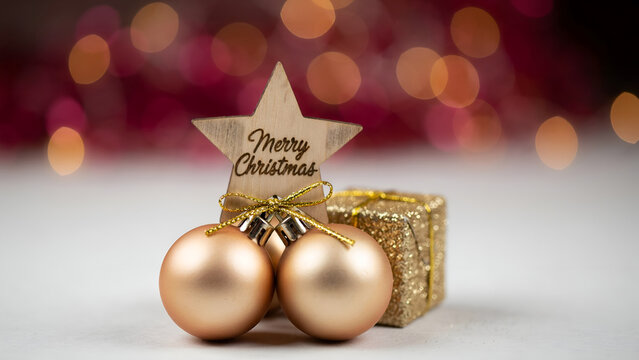 Christmas composition with golden ornaments, a wooden star with merry christmas text, and a small glittery gift box against a festive bokeh background