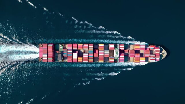 High aerial overhead tracking view of a super container cargo ship sailing over open ocean as a concept for shipping and logistics
