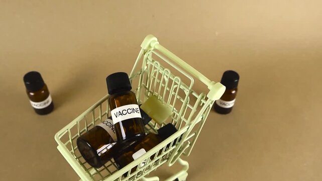 Small shopping cart carrying several brown glass bottles labeled vaccine, conceptualizing the purchase, distribution, and commercialization of immunization drugs against disease and pandemics