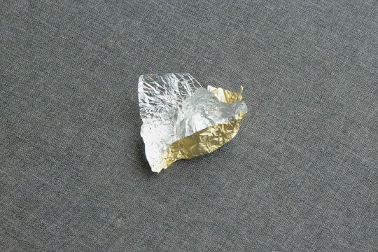 Foil wrapper crumpled on grey fabric surface in a close-up shot showing texture and colors of materials