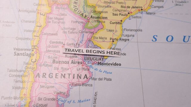 Paper label reading Travel Begins Here placed on map of South America