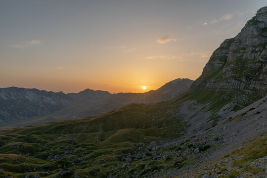 Golden sunset over a rugged alpine valley with rocky slopes and green meadows in Durmitor National Park, Zabljak Municipality, Montenegro, serene summer landscape