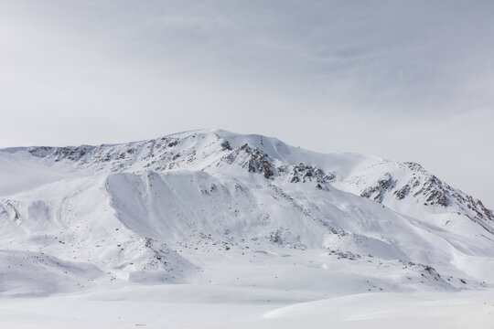Wide winter landscape on Arabel Plateau with snow-covered mountain ridges and smooth white valleys under an overcast sky, remote highland scenery in Kyrgyzstan