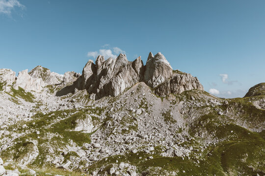 Scenic rocky mountain ridge and green alpine slopes on the hiking route to Bobotov Kuk in Durmitor National Park, Zabljak Municipality, Montenegro under clear blue sky
