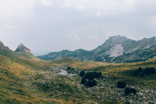 Scenic mountain panorama with rocky peaks, alpine meadow and a small lake under cloudy sky in Durmitor National Park, Zabljak, Montenegro, summer travel nature