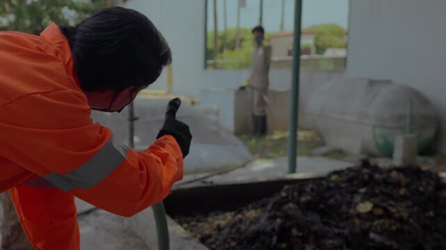 Two masked workers in overalls use a hydro pump to manage organic waste, giving a thumbs-up to start work at a circular agribusiness project.