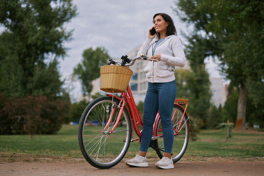 Woman talking on smartphone beside bicycle in autumn park