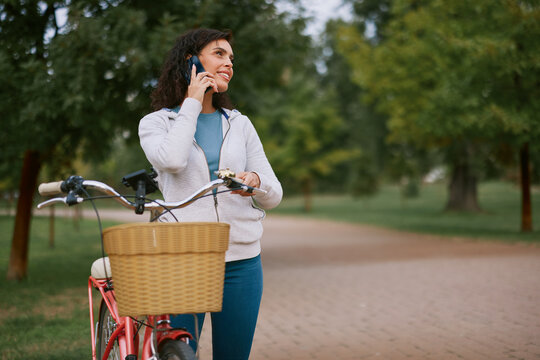 Woman checking smartphone while walking bicycle in autumn park