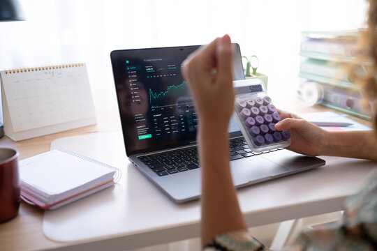 White woman calculating finances with calculator and laptop displaying