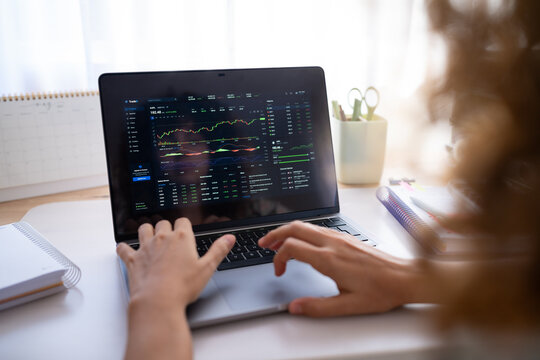 Hands typing on laptop showing stock market charts and financial data