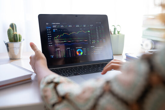 White person pointing at stock market dashboard on laptop in home