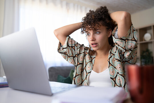 Shocked white woman using laptop at home desk in Spain