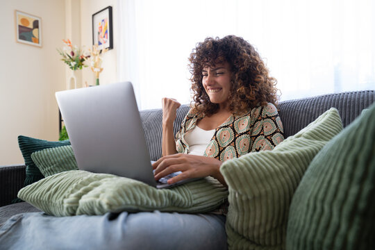 White woman cheering on a couch using laptop