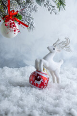 White reindeer figurine beside red Christmas ornament in snowy scene with hanging bauble for vertical New Year greeting or festive winter design © Svetlana Kolpakova