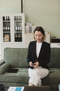 Two smiling women are comfortably sitting on a couch, sharing a moment and collaborating on a tablet, working together in a home office environment