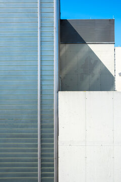 Vertical metal facade and concrete wall form sharp shadows and graphic geometry in a minimalist urban architecture detail beneath a clear blue sky