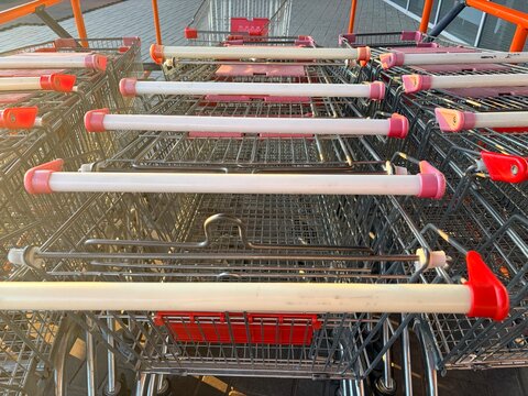 Empty metal shopping carts with red handles parked outside a modern supermarket