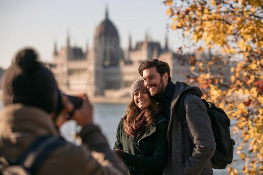 Professional photographer taking pictures of a smiling couple in Budapest during an autumn travel photo session with the Hungarian Parliament in the background