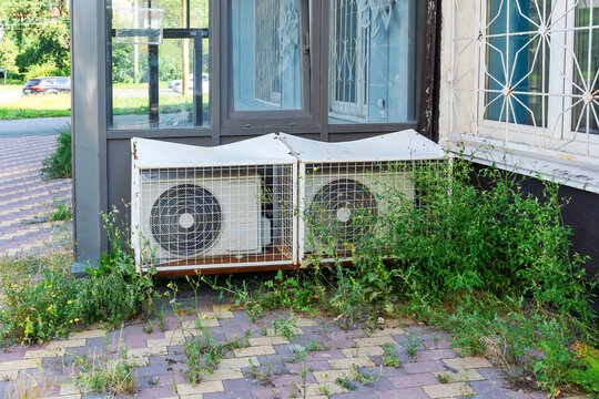 Two damaged outdoor air conditioning units in a protective lattice cage near the building.