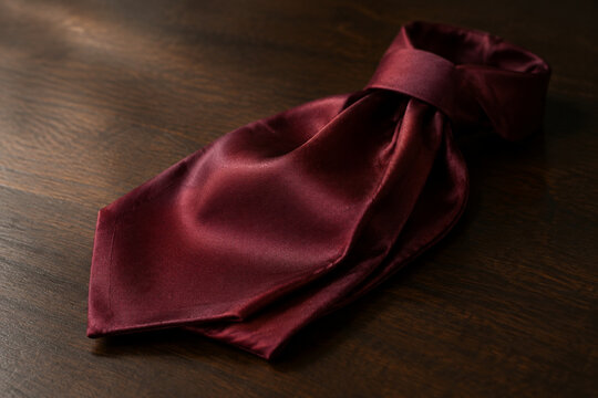 Folded burgundy silk cravat on dark wood, elegant menswear and formal fashion concept
