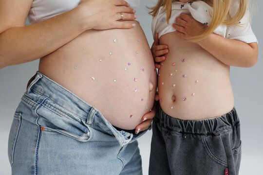 Pregnant mother and young daughter showing their decorated bellies with colorful heart and star stickers, celebrating pregnancy, motherhood, family, and the special bond between mother and child.