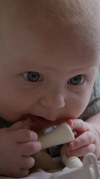 Vertical shot of Caucasian baby chewing silicone teether toy lying down. Footage suitable for parenting blogs, baby product marketing and pediatric healthcare campaigns