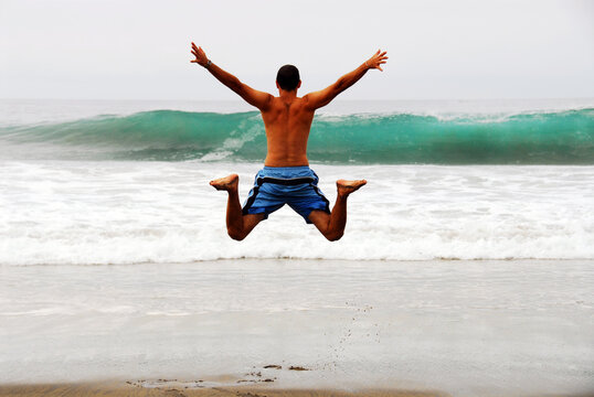 Shirtless man jumping over blue waves at the beach, Mazunte, Mexico