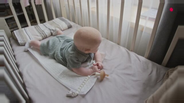 Portrait of Caucasian baby practicing tummy time inside crib and looking at camera. Footage suitable for parenting blogs, pediatric healthcare campaigns and nursery product advertising