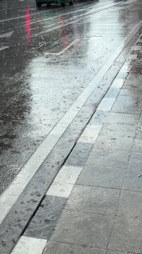 Vertical 4K video showing heavy downpour raining continuously on asphalt road surface as motor vehicles drive past.